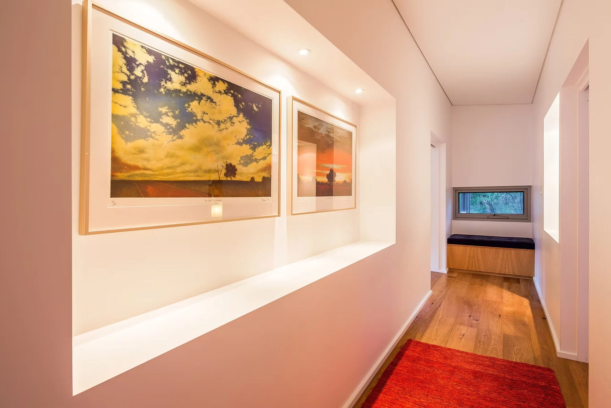 A hallway at Injidup Sanctuary displaying framed artwork, with a window seat at the end