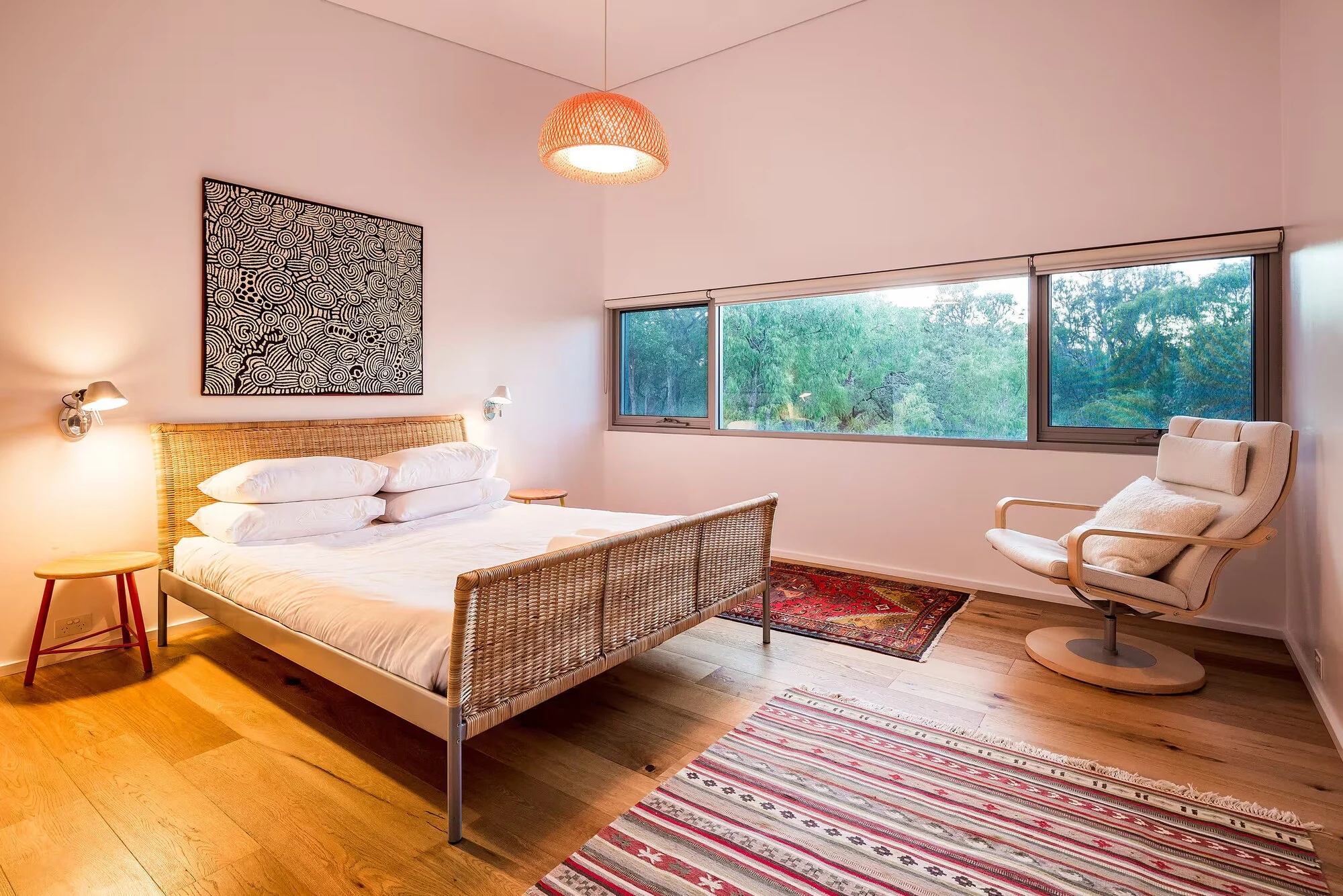 A bedroom at Injidup Sanctuary with a timber bed, white armchair, original artwork and bushland views