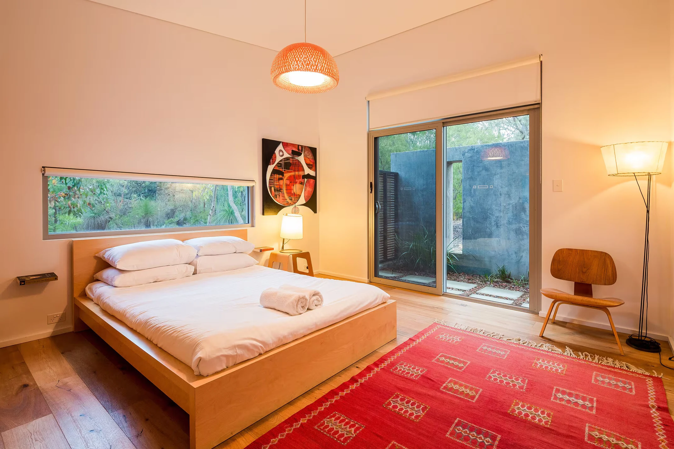 A bedroom at Injidup Sanctuary with timber furnishings, original artwork and windows overlooking native bush