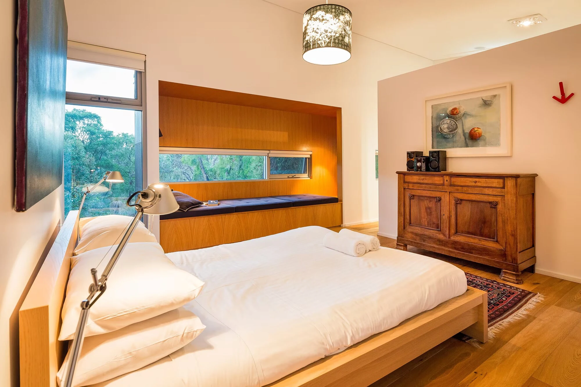 Another view of Injidup Sanctuary's bedroom, with timber furniture, artwork and a built-in window seat