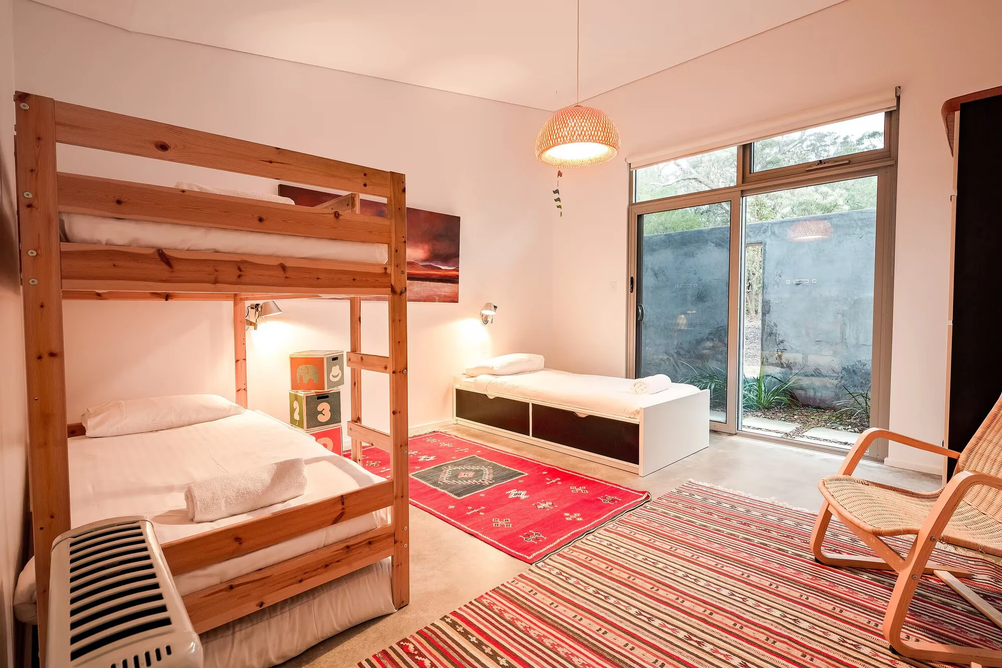 Injidup Sanctuary's bedroom with timber bunk beds, a separate single bed and sliding doors overlooking the courtyard