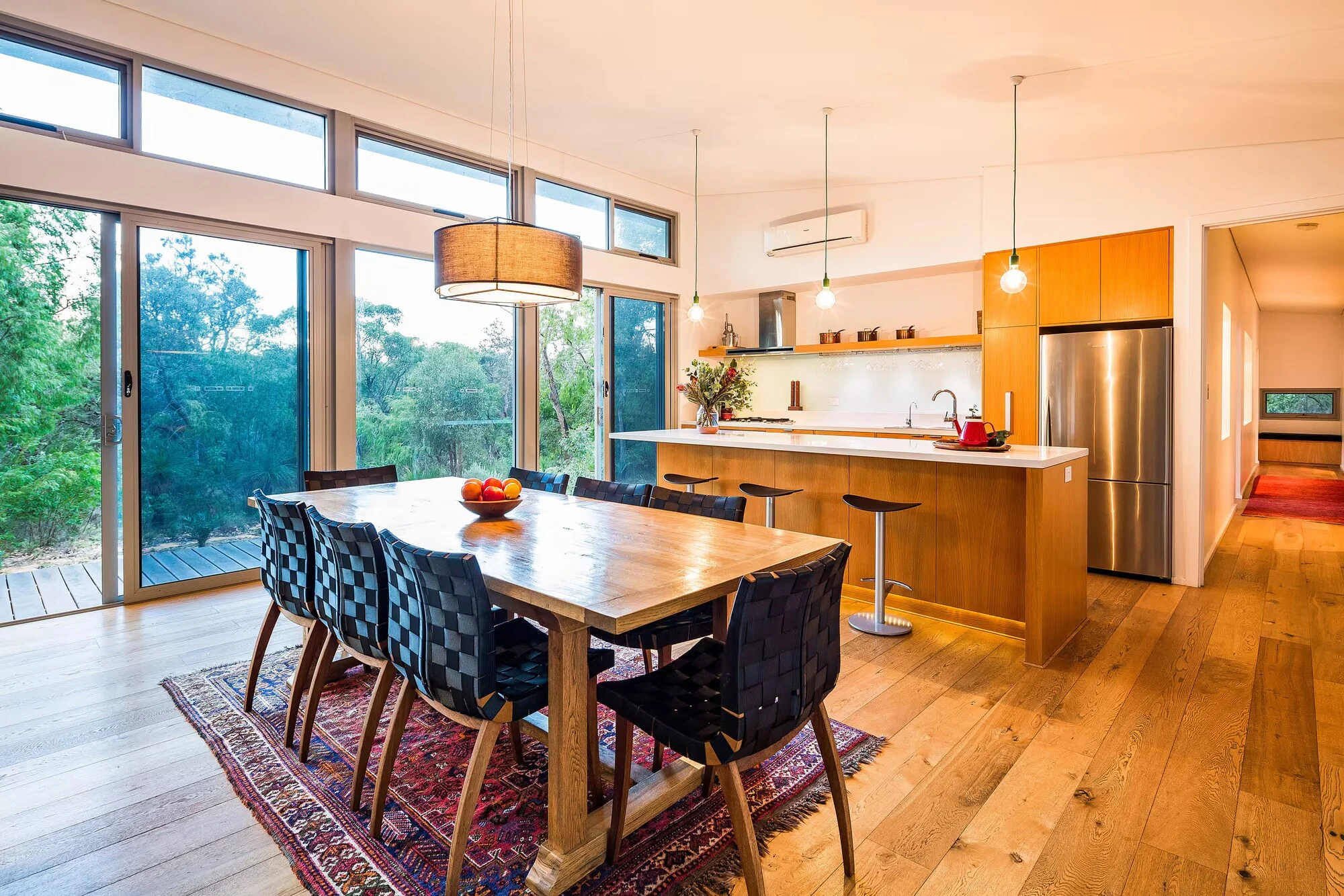 The open-plan dining room and kitchen at Injidup Sanctuary with floor-to-ceiling windows overlooking the bush