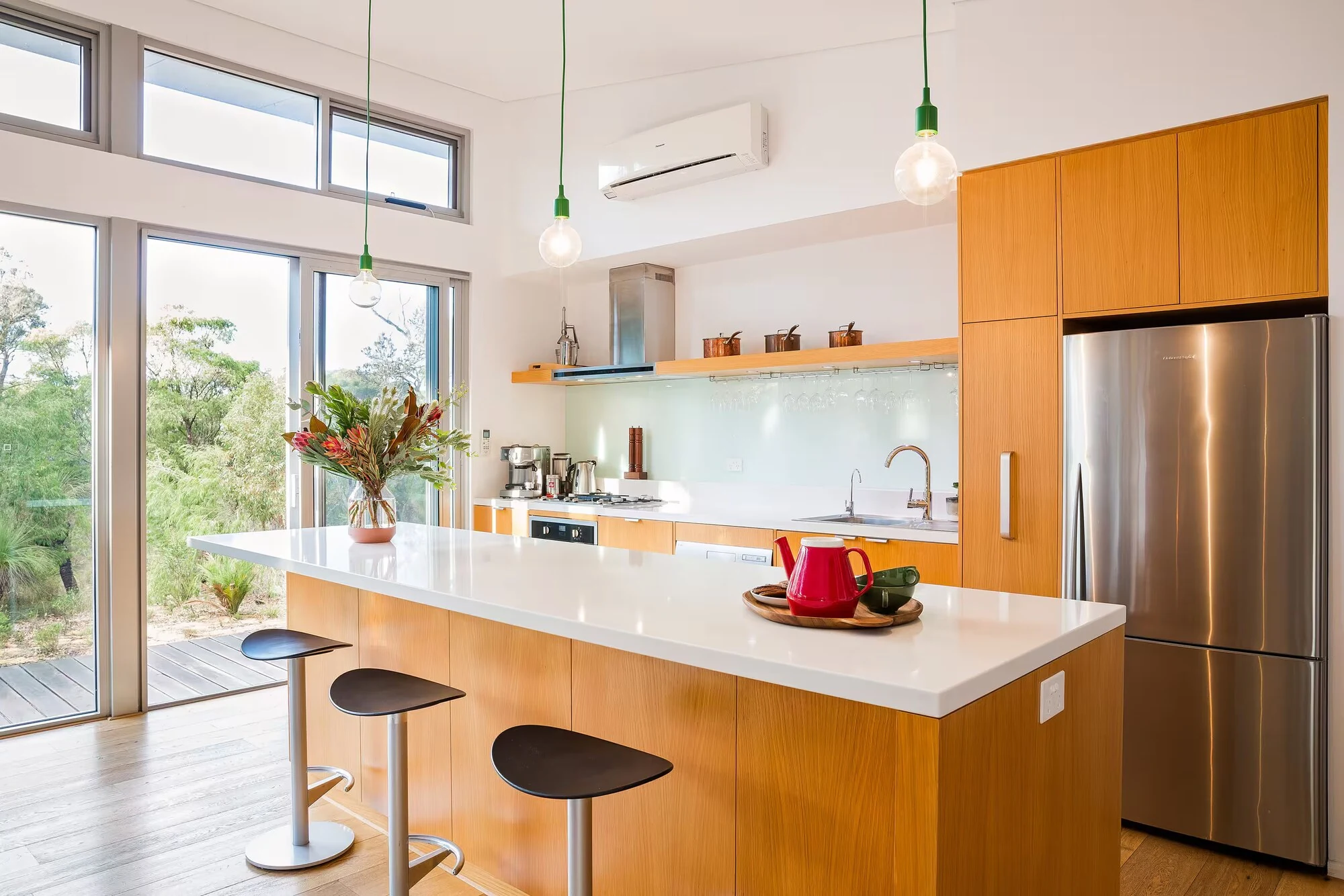 Injidup Sanctuary's light-filled kitchen with a timber island, white benchtop and views of native bushland